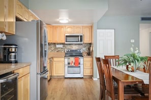 A kitchen with wooden cabinets, a stainless steel refrigerator, a microwave, an oven, and a dining table with chairs.