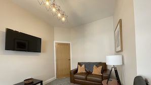 A living room with a brown leather sofa, a grey carpet, a black coffee table, a TV mounted on the wall, and a modern light fixture. - Grisedale Pike -  a maisonette that sleeps 2 guests  in 1 bedroom (Central Keswick)