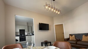 A dining area with a table set for four, a television mounted on the wall, and a kitchen visible through an open door. - Grisedale Pike -  a maisonette that sleeps 2 guests  in 1 bedroom (Central Keswick)