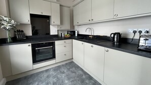 A modern kitchen with white cabinets, a black countertop, a built-in oven, a sink, and a coffee maker. - Grisedale Pike -  a maisonette that sleeps 2 guests  in 1 bedroom (Central Keswick)