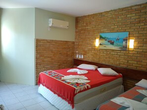 A hotel room with a brick wall, a painting of boats, a bed with a red blanket, and an air conditioning unit. - Pousada Porto do Colibri (Ipojuca)