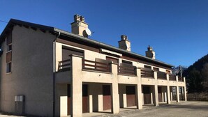 A building with multiple garage doors, a gravel driveway, and a clear blue sky. - 1st floor, tv, ski locker, 58m², Villard de Lans (Corrençon-en-Vercors)