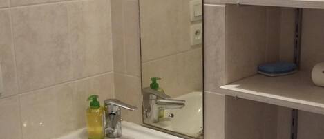 Une salle de bain avec un lavabo blanc, un miroir et des étagères.
