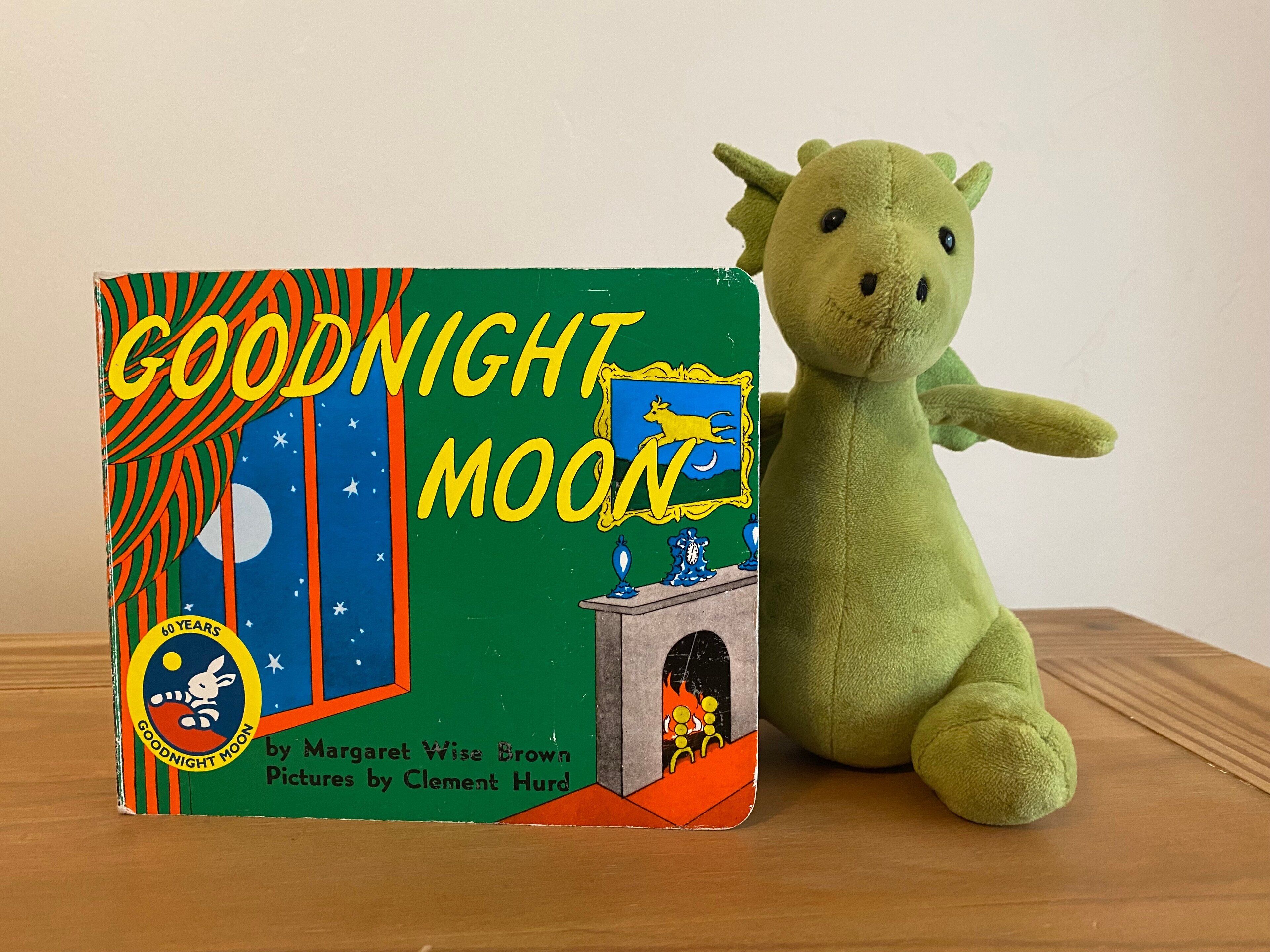 A book titled 'Goodnight Moon' next to a green plush toy.