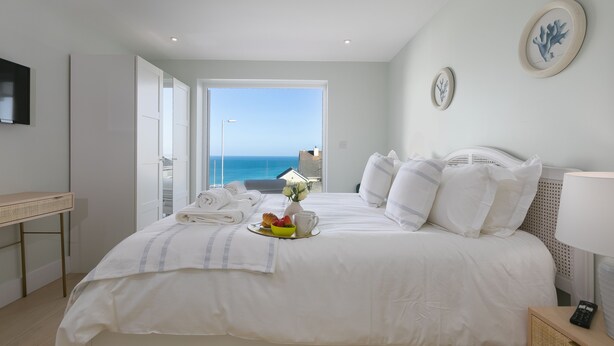 Ein Hotelzimmer mit Bett, Nachttisch, Fernseher und Meerblick.