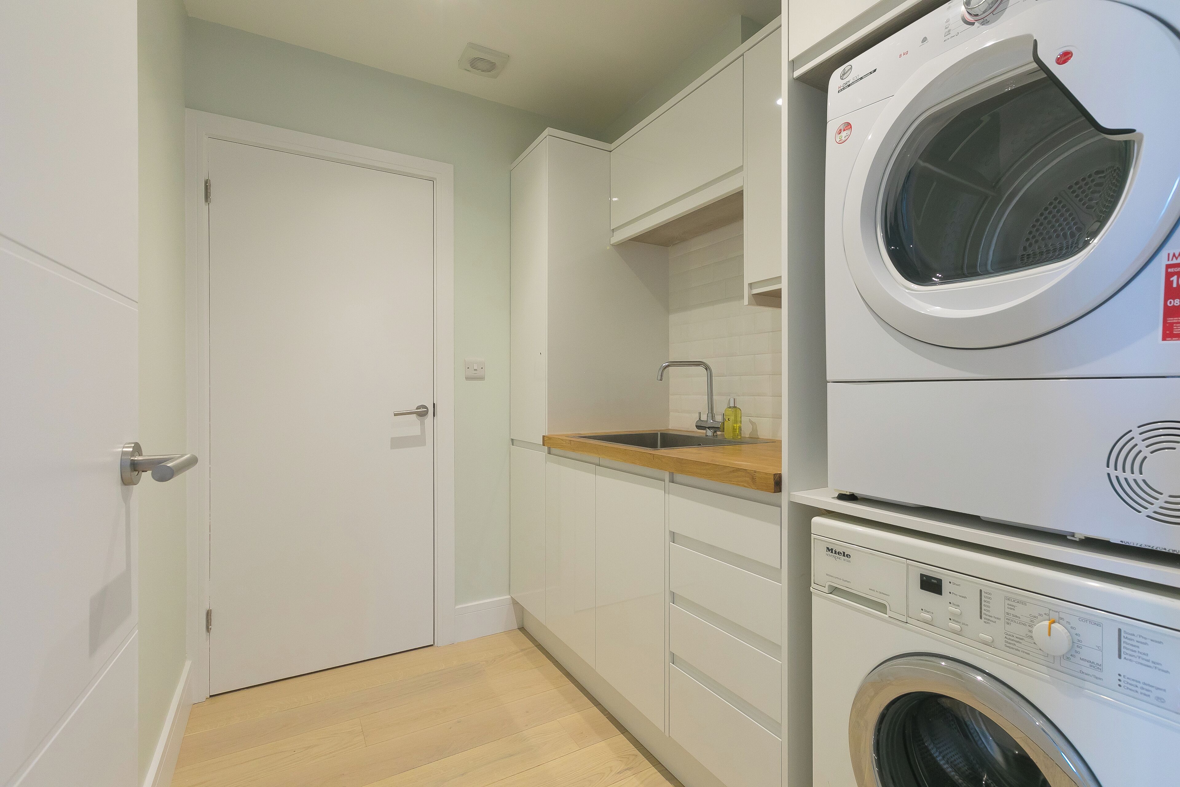 A compact laundry room with a front-loading washing machine and dryer, wooden countertop, and white cabinetry.