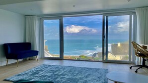 Ein modernes Wohnzimmer mit einem großen Schiebeglastür, die auf einen Balkon mit Meerblick führt.