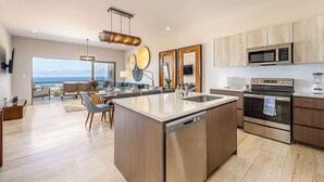A modern kitchen with a central island, stainless steel appliances, and a view to the outside. - Punta Serena | Los Tules Oceanview Penthouse Condo (Residencial Los Tules)