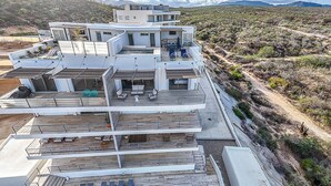 A multi-story modern house with a rooftop deck, large windows, and a view of a mountainous landscape. - Punta Serena | Los Tules Oceanview Penthouse Condo (Residencial Los Tules)