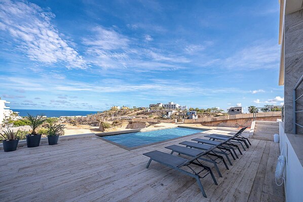 A rooftop pool area with lounge chairs, a small pool, and a view of the coastline.