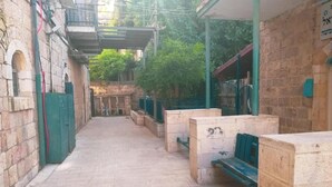 Un estrecho callejón con paredes de piedra, bancos y una zona cubierta con techo metálico.