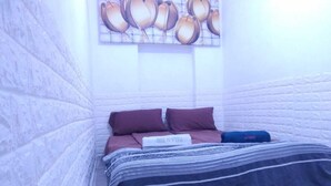 Una habitación pequeña y estrecha con una cama, almohadas y una obra de arte colgada en la pared.
