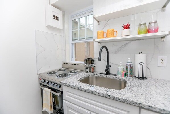 Kitchen features a gas stove, stainless steel sink, and white cabinetry.