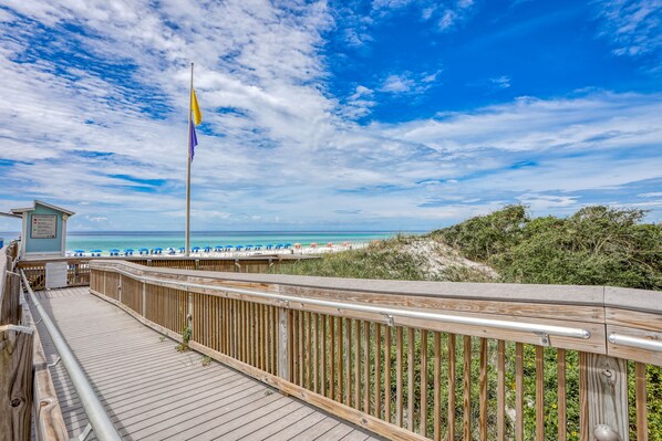 Walk along the boardwalk to the beach, where a flagpole stands tall and lifeguards are on duty.