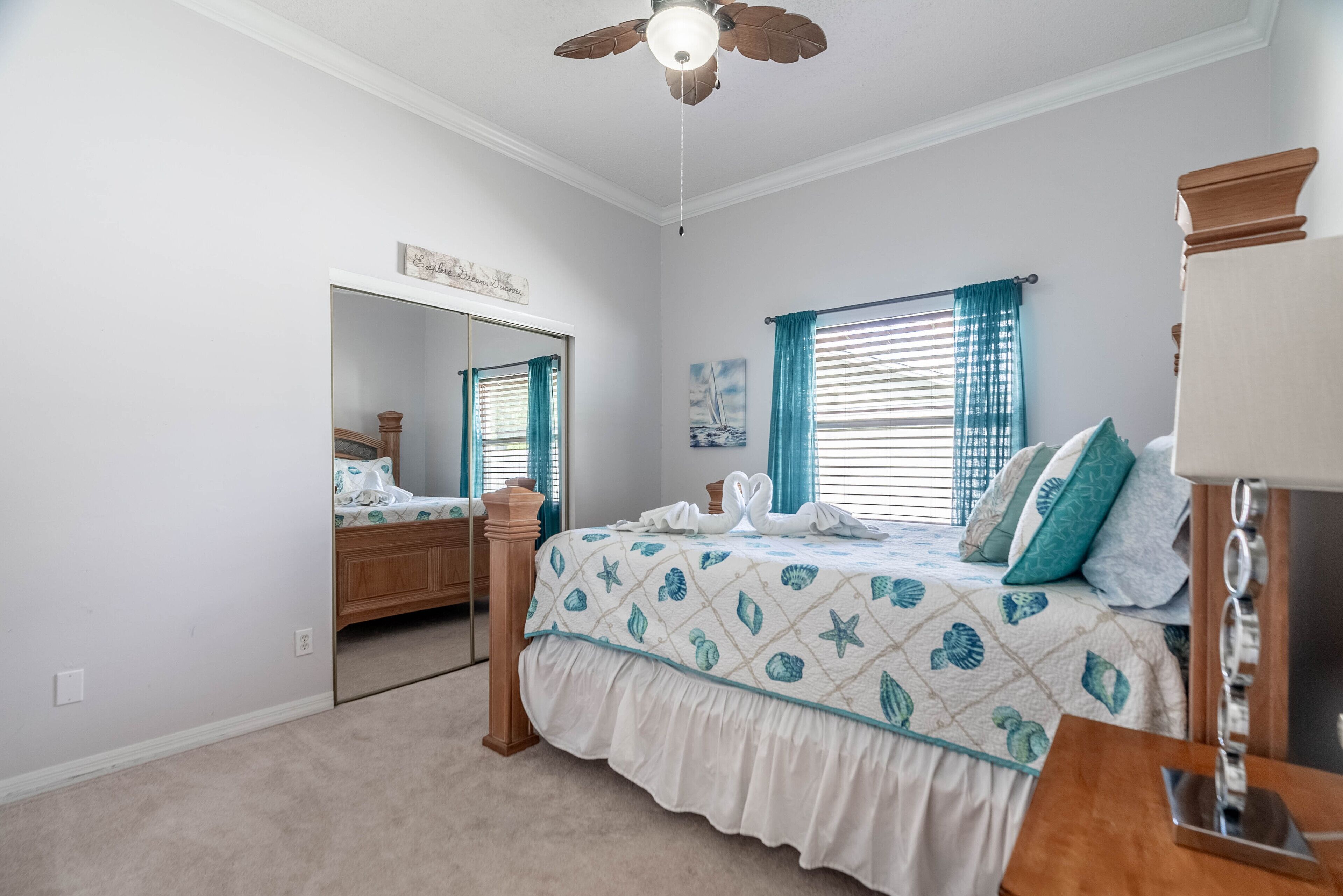 A bedroom with a bed, a dresser, a mirror, a ceiling fan, and a window with curtains.