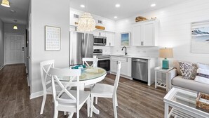 Una cocina moderna con muebles blancos, electrodomésticos de acero inoxidable y una mesa redonda de vidrio con sillas blancas.