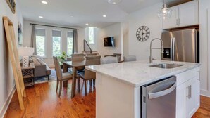 A modern kitchen with a central island, stainless steel appliances, and a dining area with a staircase leading to an upper level.