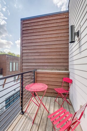 Une terrasse en bois avec une rambarde en métal, deux chaises rouges et une petite table ronde.