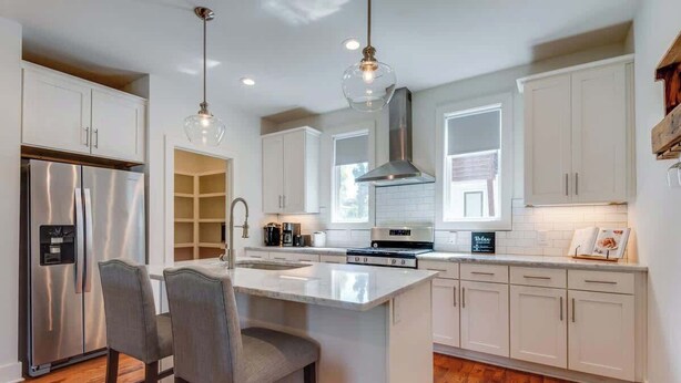 A modern kitchen with white cabinets, a stainless steel refrigerator, a central island with bar stools, and pendant lighting.