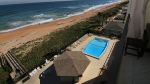 A view of a beach with a swimming pool and lounge chairs.