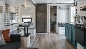 Una cocina compacta con una isla central, un área de comedor con sofá y vista hacia un dormitorio.