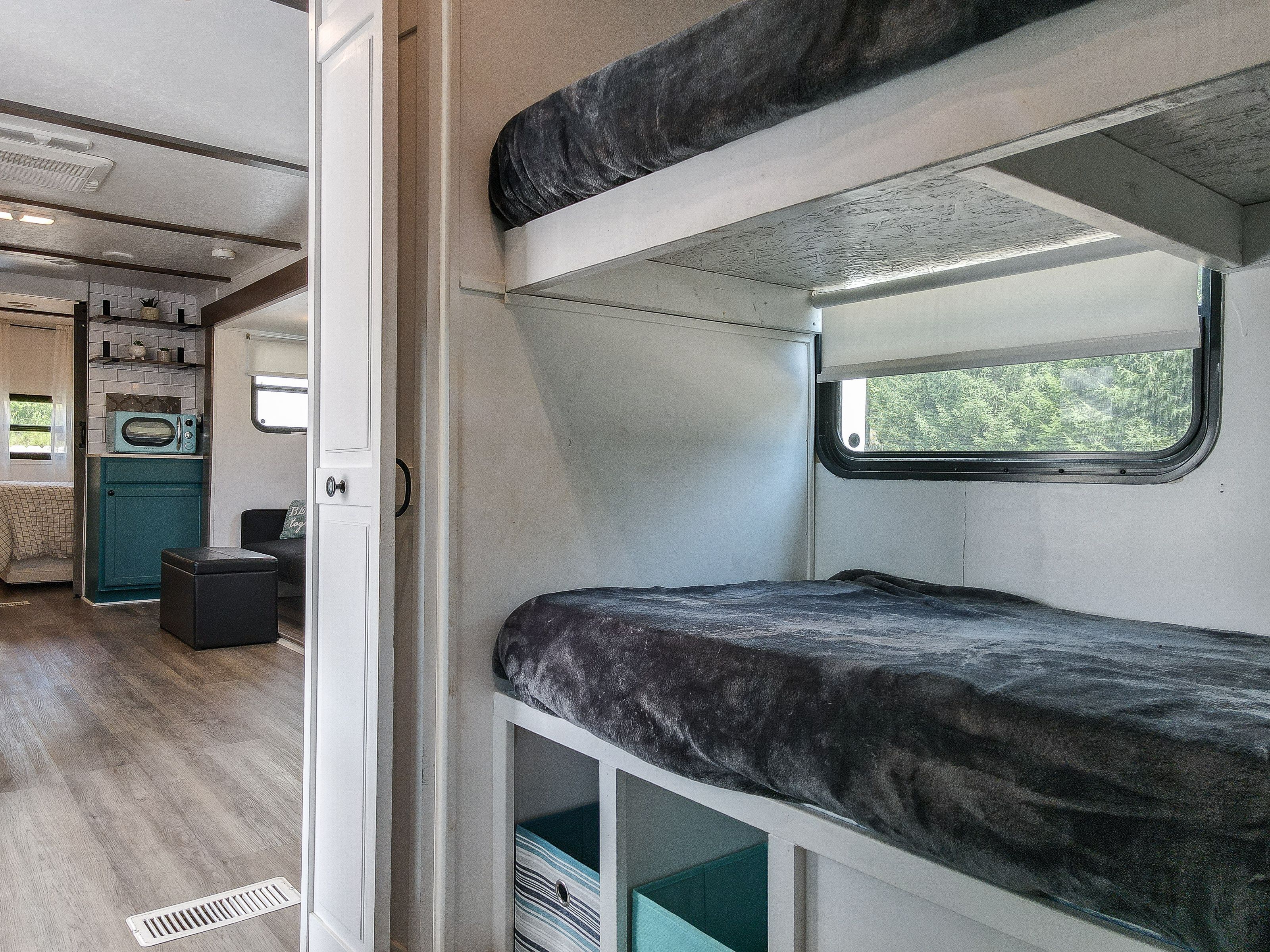 Interior d'una caravana compacta amb cuina americana, zona de dormir amb finestra i un petit espai per seure.