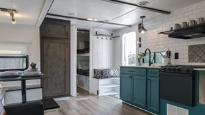 Una cocina moderna con armarios azul verdoso, una estufa negra y un ventanal con vistas a un jardín.