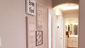 Un pasillo con cuatro frases inspiradoras enmarcadas en la pared, que conduce a un baño con espejo y lavamanos.