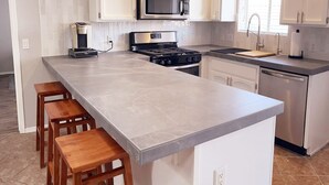 Una cocina moderna con armarios blancos, una isla grande con taburetes, electrodomésticos de acero inoxidable y un ventanal que aporta luz natural.