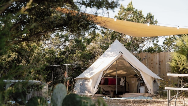 Een tent met een bed, omringd door bomen en een houten hek.