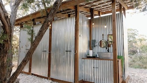 Een rustieke hut met een houten pergola, golfblikken wanden en een grindpad.