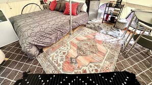 Een tent-accommodatieruimte met een bed, een klein tafeltje, een stoel, een koffiezetapparaat en een vloerkleed.