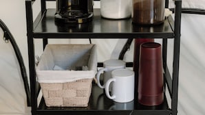 Een zwart metalen schap met diverse keukenbenodigdheden, waaronder een koffiezetapparaat, mokken en servies.
