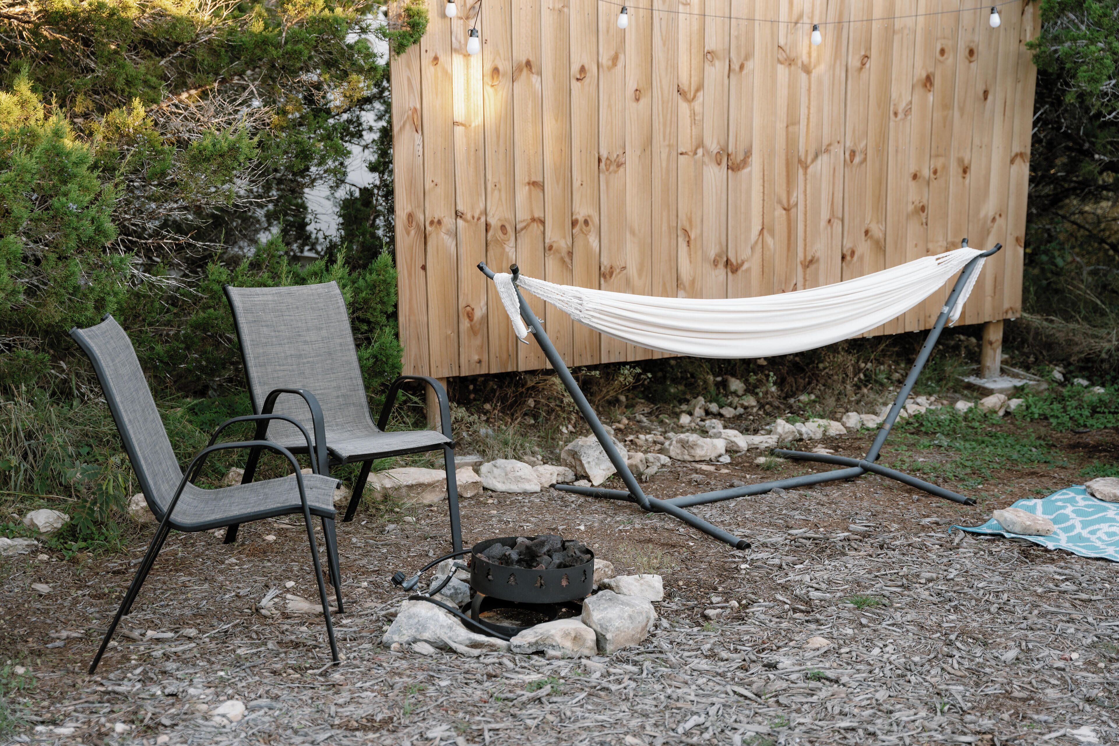 Een hangmat, twee stoelen en een vuurkuil in een buitenomgeving.