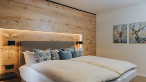 Une chambre à coucher moderne avec une tête de lit en bois, un grand lit avec de nombreux oreillers et deux tableaux accrochés au mur.