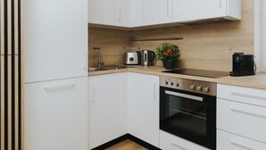 Une cuisine moderne avec des armoires blanches, une cuisinière en acier inoxydable, un four encastré, une machine à café et une bouilloire posées sur le plan de travail.