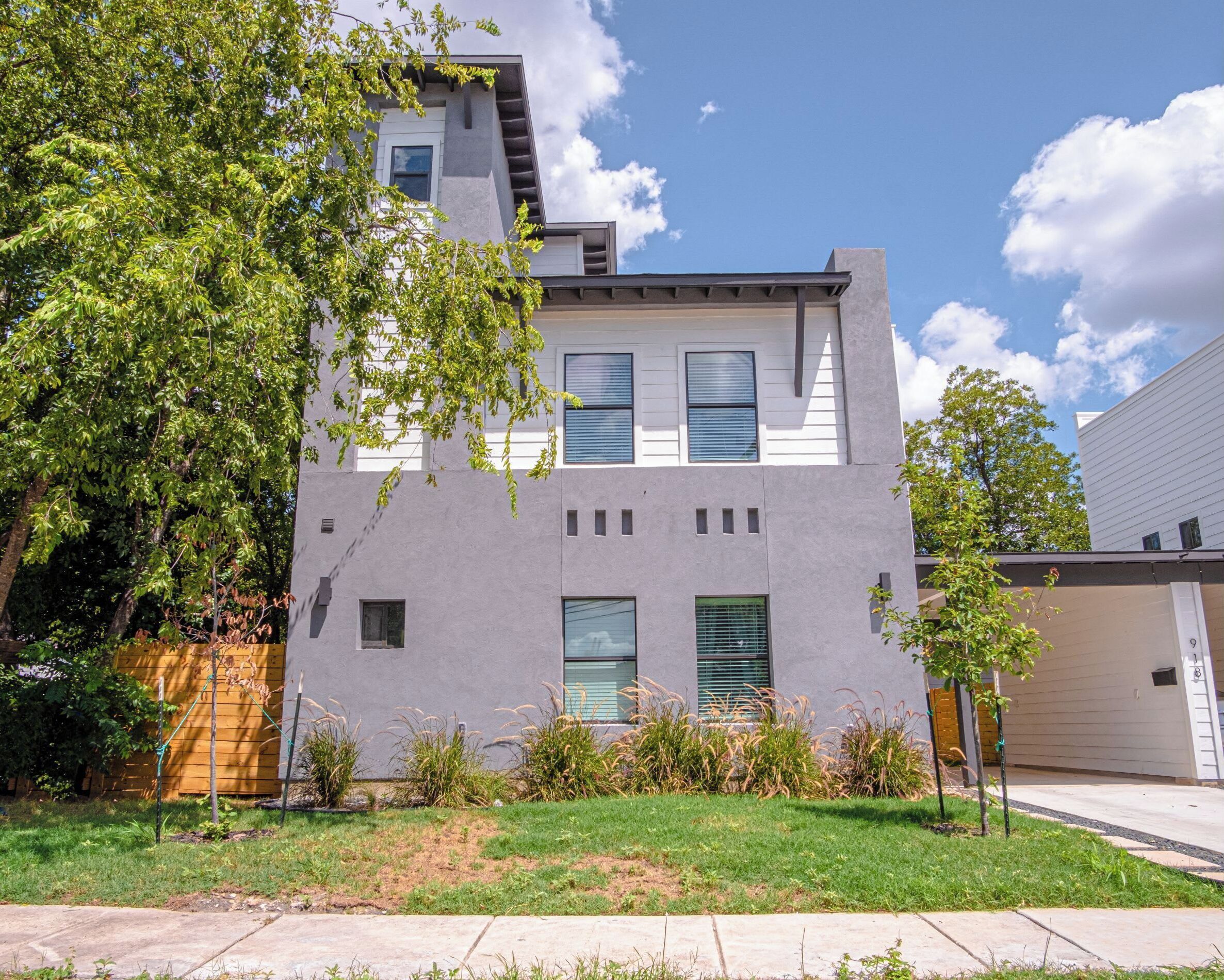 A modern two-story residential building with a flat roof, large windows, and a well-maintained lawn.