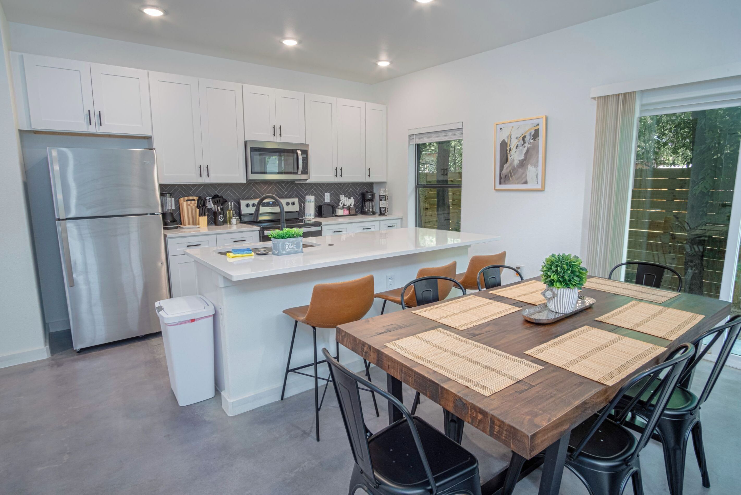 A modern kitchen with white cabinets, stainless steel appliances, and a wooden dining table with black chairs.