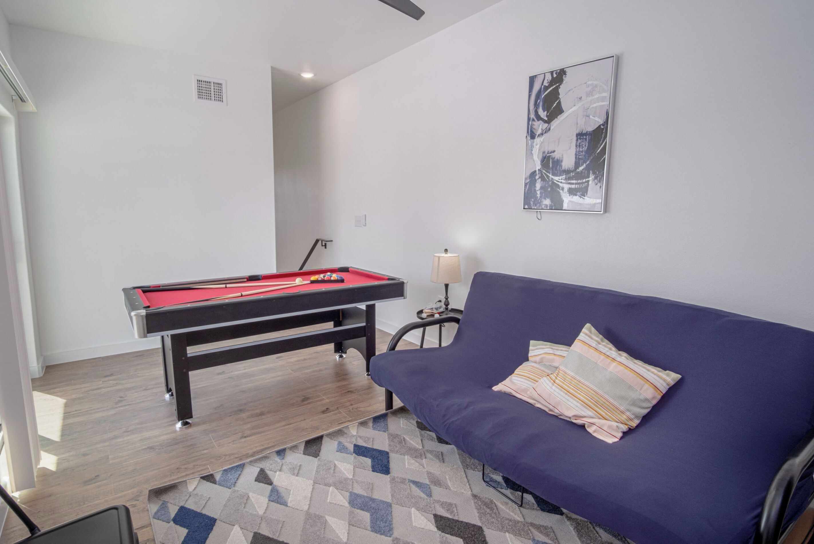 Ein Zimmer mit Billardtisch, einem blauen Sofa, einem gemusterten Teppich und einem gerahmten abstrakten Gemälde an der Wand.