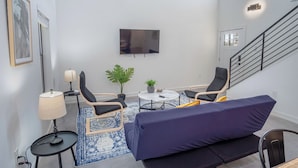 Una sala de estar moderna con un sofá, dos sillones, una mesita, un televisor y una escalera.