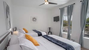 Habitación de hotel con dos camas, ventilador de techo, televisión y ventana con cortinas.