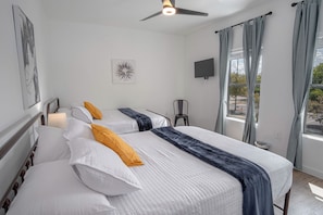 Two beds with dark blue throw blankets, a flat-screen TV, and a ceiling fan are featured in this stylish room.