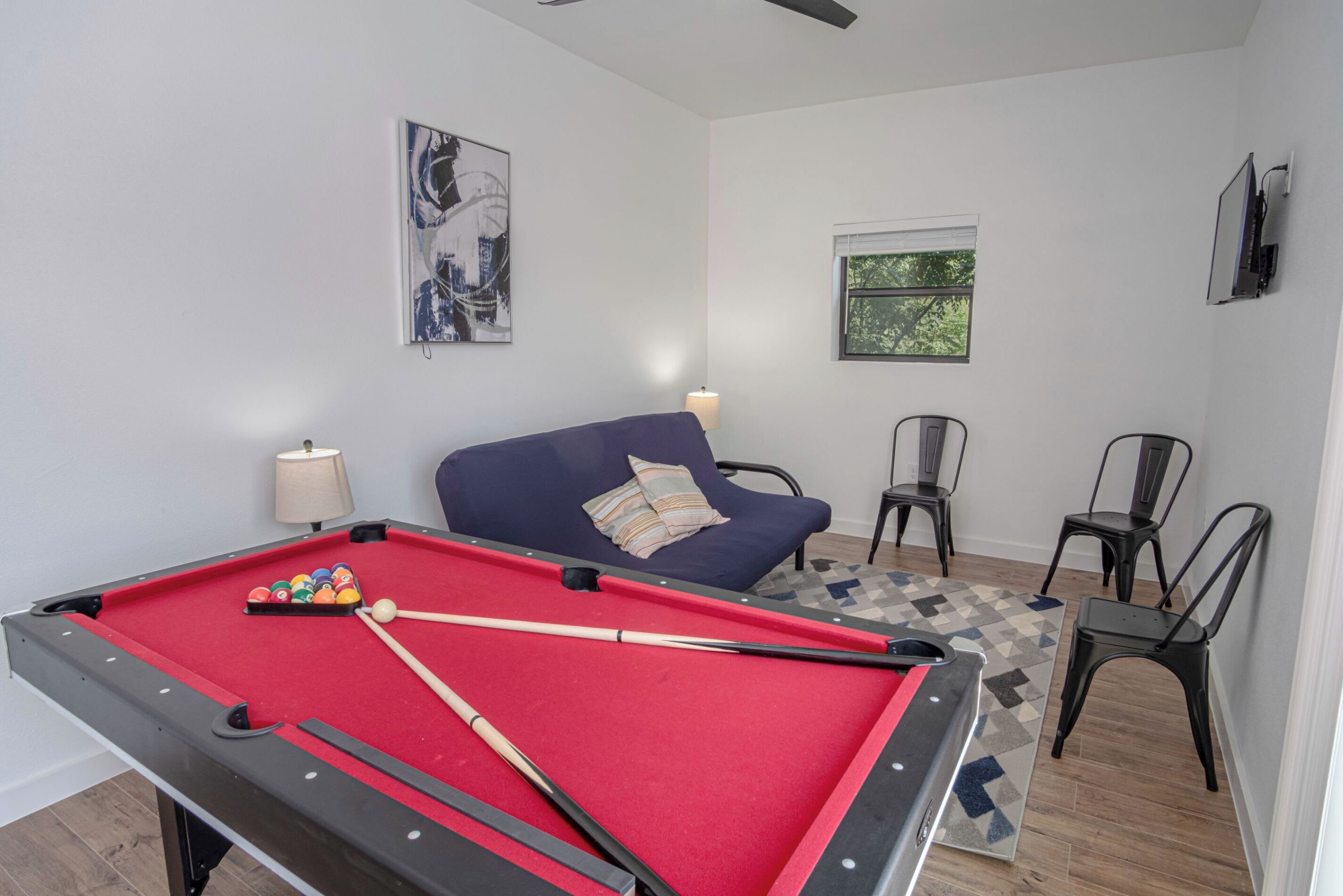 Een biljart met ballen, een bank en een televisie in een kamer met witte muren en een raam.