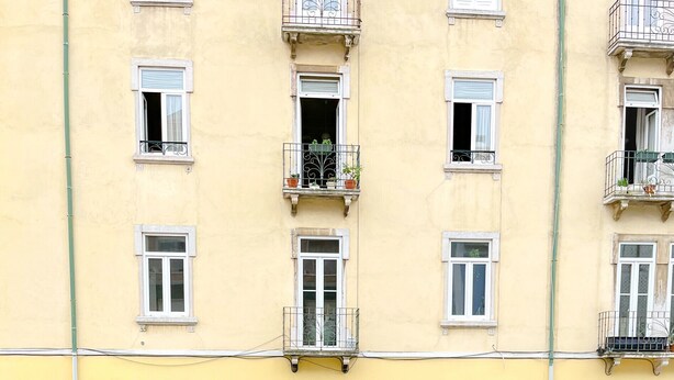 A balcony with two wooden chairs and a small table, overlooking a yellow building with multiple windows and balconies. - FLH Marquês Pombal Flat with Balcony (Lisbon)