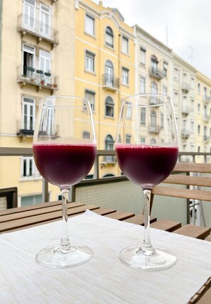 Zwei Weingläser auf einem Holztisch mit Blick auf gelbe Gebäude vom Balkon aus.