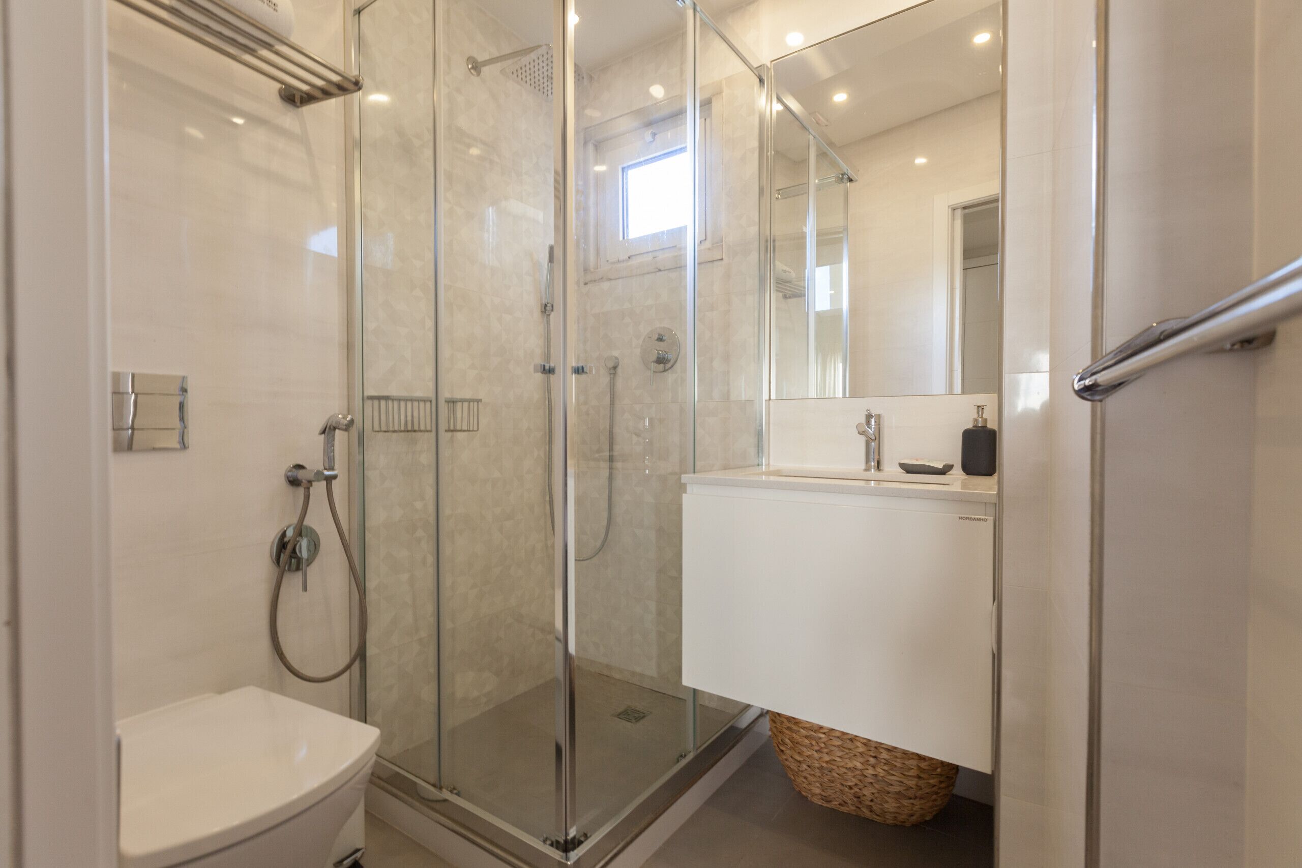 Un baño moderno con ducha envuelta en vidrio, un lavabo blanco y un espejo sobre él.