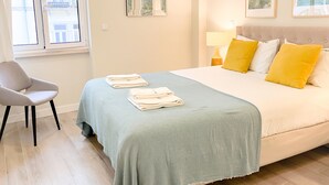 A neatly arranged bedroom with a bed, a chair, and two windows. - FLH Marquês Pombal Flat with Balcony (Lisbon)