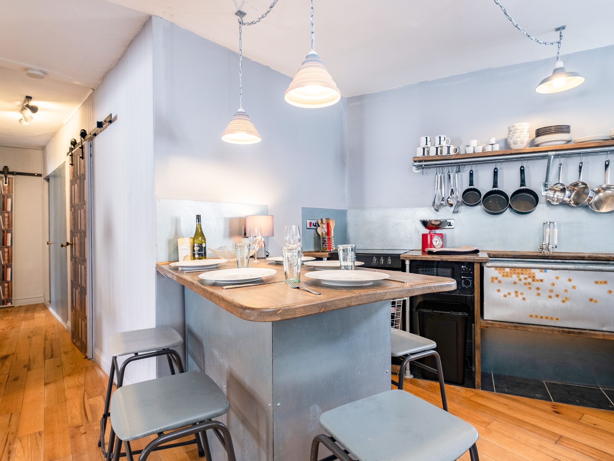 A compact kitchen with a central island, bar stools, and hanging pots.