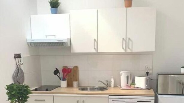 A compact kitchen with white cabinets, a sink, a dishwasher, and a dining area with a table and chairs. - Agréable F2 Proche Gare (Le Mans)
