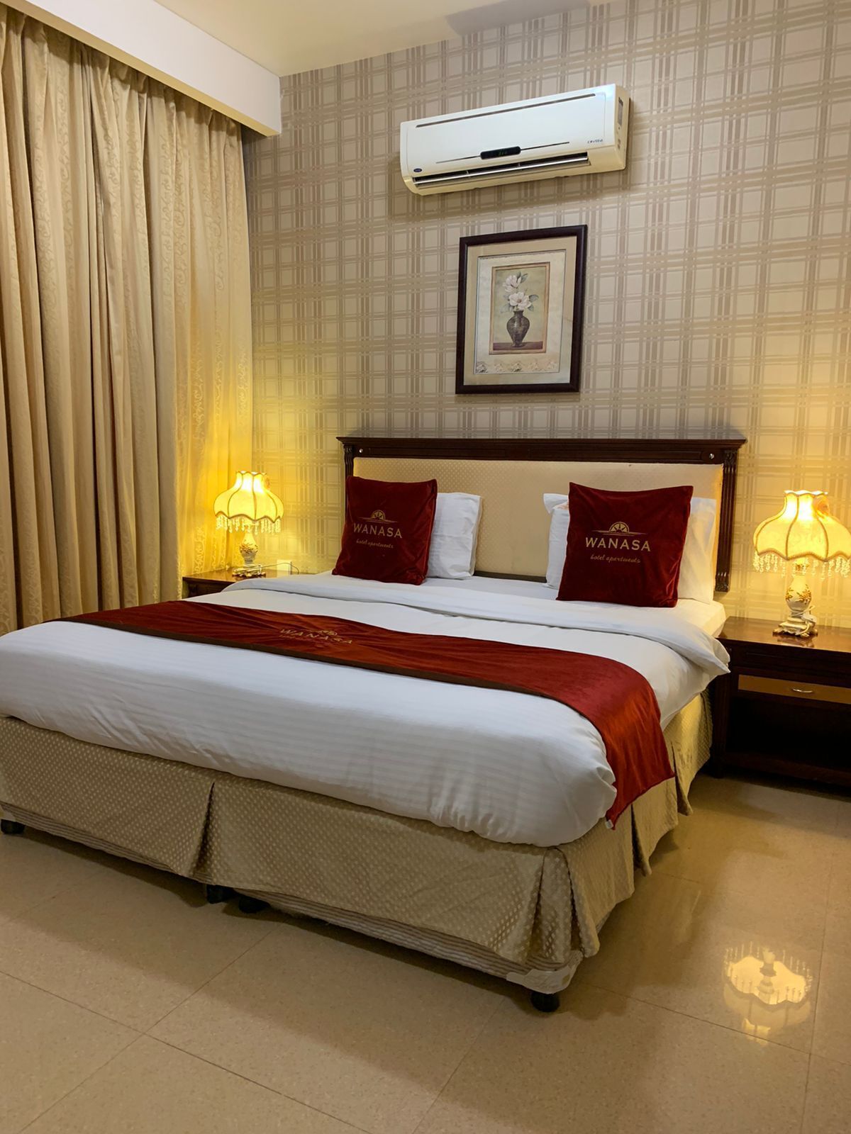 Quarto de hotel com uma cama grande, duas almofadas com o nome do hotel, um ar condicionado, um quadro na parede e duas luminárias de cabeceira.